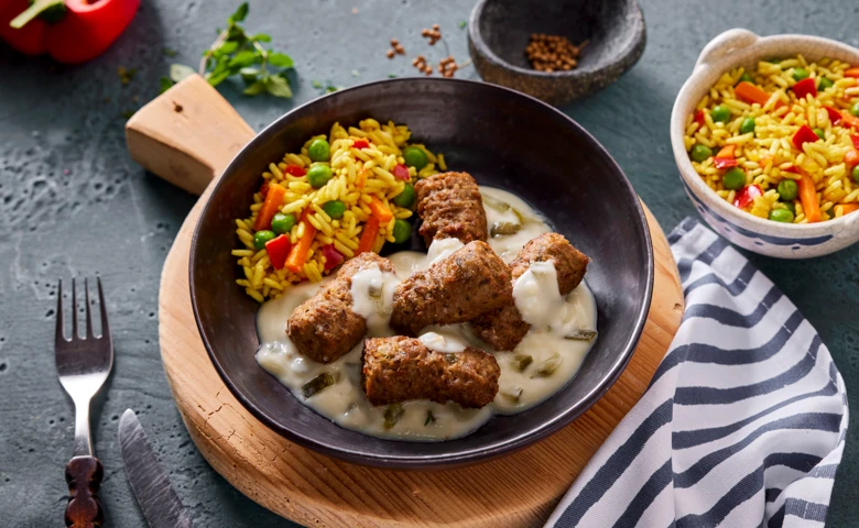 Cevapcici in Tzatzikisoße Hackfleischröllchen vom Rind in cremiger Tzatzikisoße mit Gurkenstreifen dazu Djuvecreis